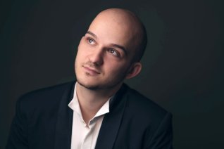 Ein Portr&auml;t des Dirigenten vor dunklem Hintergrund.